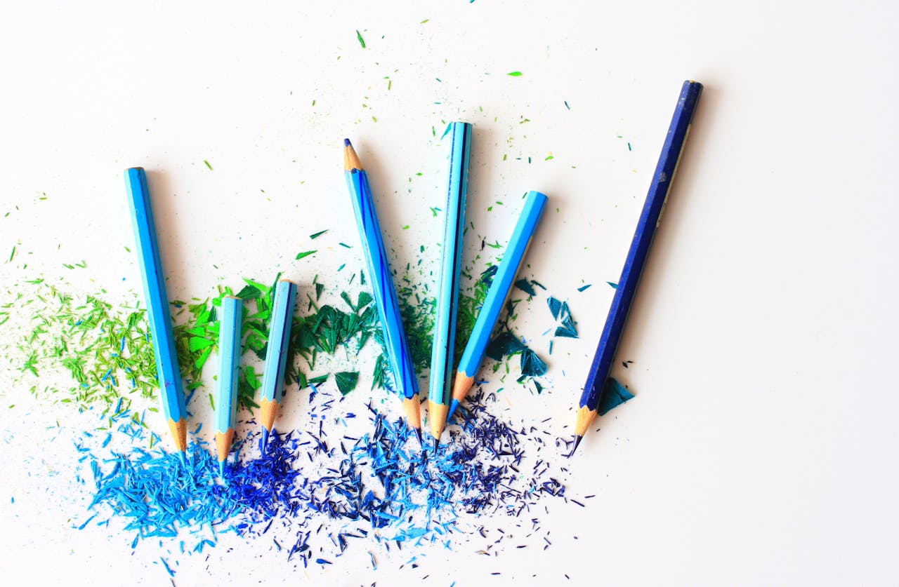 Home Creative display of colored pencils and vibrant shavings on a white background.